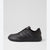 A black low-top sneaker shown from the side against a light gray studio background. The shoe features a matte black leather upper with three darker gray stripes on the side, black laces, and a thick black sole.