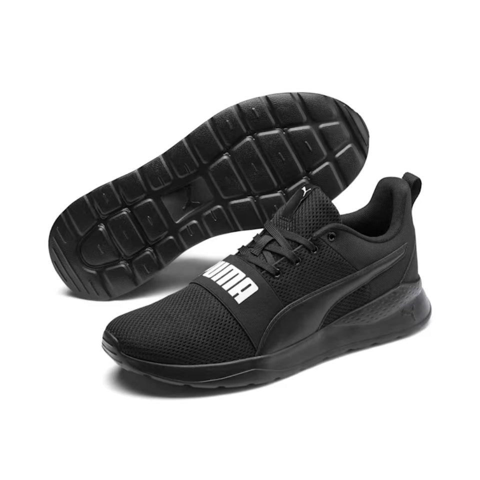 A pair of black Puma sneakers, with one shoe showing its textured black outsole and the other showing the side profile with the white Puma logo on the side strap.