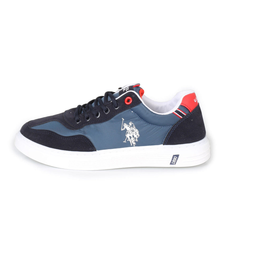 A low-top sneaker in navy blue suede and mesh with a slate blue side panel, white laces, a white midsole, and red accents on the heel and tongue, shown against a plain white background.
