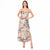A woman modeling a sleeveless maxi dress with thin straps and an allover abstract floral print in beige, black, and brown tones, standing against a plain white background.