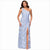 A woman modeling a floor-length one-shoulder gown with a high front slit. The dress has a light blue base with a textured, raised floral pattern in pale blue and white.