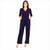 A woman modeling a dark purple wrap-style jumpsuit with three-quarter sleeves, side pockets, and a self-tie belt, shown against a plain white background.