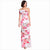 A woman modeling a floor-length off-the-shoulder maxi dress with a pink and red floral print on a white background, set against a plain white studio backdrop.