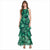 A woman modeling a sleeveless, high-neck, tiered maxi dress with a green and black floral pattern, set against a plain white background.