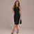 A woman modeling a sleeveless black midi dress with lace detailing at the neckline and hem, paired with black strappy heels and holding a small black handbag against a plain beige studio background.