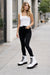 Woman wearing a white tank top, black pants, and white boots on a city street.