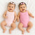 Two smiling babies lying side by side on a white textured blanket, wearing matching pink sleeveless bodysuits and pink bow headbands.