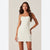A woman modeling a strapless off-white bodycon mini dress with a scalloped neckline, photographed against a plain light beige studio background.