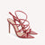 A pair of red patent leather strappy high-heeled sandals with pointed toes and slim stiletto heels, shown on a light off-white background.