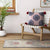 Decorative pillow on a wooden bench with a plant and rug in the background