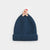 A dark blue ribbed knit beanie hat featuring a small gingerbread man ornament wearing a red Santa hat on top, set against a plain light gray background.