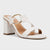 A white leather block-heel mule sandal with crisscrossing straps, a gold-tone metal ring detail, and a square toe, shown on a light gray background.