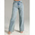 A person wearing light-wash blue high-rise wide-leg jeans with a faded wash, paired with white heeled sandals, shown against a plain light gray studio background.