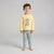 A young boy stands barefoot against a light gray studio background, wearing a pale yellow long-sleeve pajama top with a cartoon rabbit graphic and mint green patterned pajama pants.