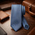 A blue and white checkered necktie displayed on a dark wooden desk alongside brown leather accessories, including a wallet, briefcase, and watch.