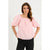A woman modeling a light pink off-the-shoulder blouse with voluminous puff sleeves and black pants, set against a plain light gray studio background.