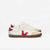A pair of Veja low-top sneakers in off-white leather with beige suede overlays, a red logo, and a brown gum sole, shown against a plain white background.