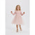 A young girl with blonde hair stands against a light gray studio background wearing a light pink long-sleeve dress with a tulle skirt, white tights, and pink shoes.