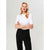 A blonde woman modeling a white short-sleeve mock neck top paired with black trousers, standing against a light gray studio background.