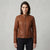 A woman modeling a brown leather motorcycle jacket with a zip-up front, stand collar, and belted waist, paired with dark jeans against a neutral gray studio background.
