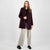 A woman modeling a dark burgundy wool-blend blazer over a black top and light beige wide-leg trousers, paired with black loafers, against a light gray studio background.