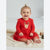 A baby girl sitting on a cream knit blanket wearing a festive red long-sleeve dress with a tulle skirt and a reindeer face applique on the chest.