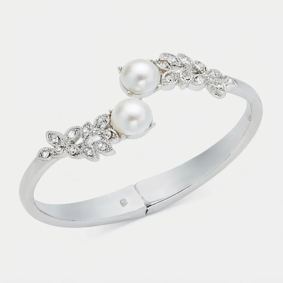 A silver-toned hinged cuff bracelet featuring two white pearls and diamond-encrusted floral motifs on each side, shown on a light gray background.