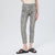 A model wearing slim-fit ankle-length pants with a gray and black snakeskin pattern, paired with black slide sandals and a beige top, shown against a plain light gray studio background.