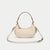 A cream-colored leather crescent-shaped shoulder bag with a top handle and a detachable shoulder strap, featuring gold-tone hardware, shown against a light gray background.