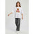 A young girl modeling an oversized white t-shirt with a brown teddy bear graphic holding a pink heart, paired with gray wide-leg jeans and white sneakers, against a light gray studio background.