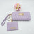 A light purple quilted wallet set with a wristlet strap and a matching card holder, featuring gold-tone hardware and a gold 'bebe' logo plaque, displayed on a white background with a small pink flower decoration.