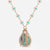 A rose gold necklace with a teardrop pendant featuring a light green stone, blue gem accents, and small clear crystals, shown on a light gray background.