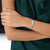 A close-up of a person wearing a polished silver cuff bracelet with a small engraved symbol, paired with a dark green satin top.