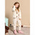 A young girl stands in a room wearing a cream-colored fleece pajama set with a teddy bear print, matching cream sweatpants, and pink slip-on boots.