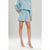 A model wearing a light blue two-piece set consisting of a long-sleeve top and matching shorts with a subtle white pattern, paired with white strappy high-heeled sandals against a light gray studio background.