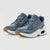 A pair of low-top sneakers with a blue denim-like textured upper, blue laces, a thick white midsole with a visible air pocket, and a gum brown outsole, shown on a light gray background.