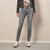 A model wearing gray slim-fit jeans, a dark gray suede jacket, a white crop top, and off-white sneakers, standing against a textured beige wall.