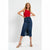 A woman modeling a dark blue denim midi skirt with a front slit, paired with a red sleeveless top and beige heeled sandals, against a plain white studio background.