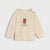 A cream-colored long-sleeve baby sweater with a teddy bear graphic wearing a red Santa hat and the text 'my first Christmas' on the chest. The top features two gold snap buttons on the shoulder.