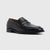 A single black leather penny loafer with a low stacked heel, shown from a three-quarters angle on a light gray background.