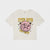 An off-white cropped t-shirt featuring a graphic print of a leopard inside a pink circle with the text 'STEP INTO the Wild' in yellow, displayed on a light gray background.