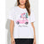 A woman wearing a white short-sleeve t-shirt with a watercolor-style graphic of a pink car carrying Christmas presents and a tree, with 'Merry Christmas' printed below.