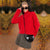 A woman wearing a bright red turtleneck sweater, a gray pleated mini skirt, black sunglasses, and a beige headband, carrying a black crocodile-embossed crossbody bag in an autumn park setting.