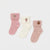 Three pairs of baby socks laid flat on a light gray background: a pink sock with a squirrel patch, an off-white sock with a grape patch, and a dusty pink sock with a peach patch.
