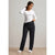 A woman modeling a two-piece pajama set consisting of a white long-sleeve henley top and dark navy pants with a white snowflake pattern, paired with white slippers.