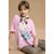 A young girl sits against a solid tan studio background wearing an oversized light pink graphic T-shirt with a large white and green floral print, leopard-print pants, and a patterned neck scarf.