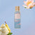 Victoria's Secret Lotus Cloud FrAGRANCE MIST bottle with a gold cap and light blue label, set against a soft blue background with decorative pear, ice cream, and lotus flower illustrations.
