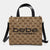 A structured tote bag with a beige and brown monogram pattern, black leather handles and shoulder strap, and gold-tone hardware. The front features the text 'bebe los angeles' in black.