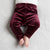 A close-up of a baby's lower body wearing plush, deep burgundy velvet pants, lying on a textured light gray blanket.