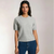 A woman modeling a light gray short-sleeve crewneck knit top with dark blue jeans, standing against a light beige studio background.